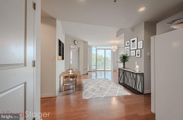 hallway featuring a notable chandelier, baseboards, visible vents, a wall of windows, and wood finished floors