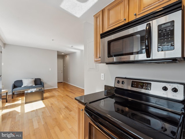 kitchen with light wood-type flooring, black range with electric stovetop, and dark stone countertops