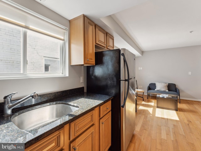 kitchen with black refrigerator, sink, dark stone counters, and light hardwood / wood-style floors