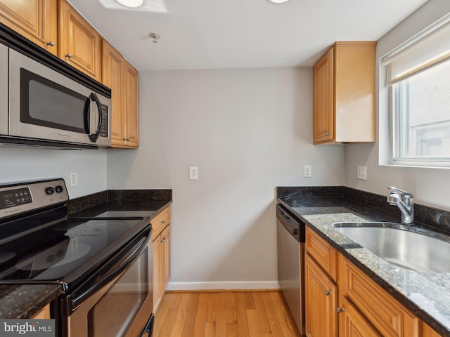 kitchen with dark stone counters, sink, stainless steel appliances, and light hardwood / wood-style floors