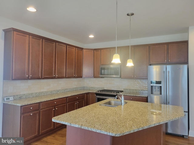 kitchen with light stone counters, sink, stainless steel appliances, and an island with sink