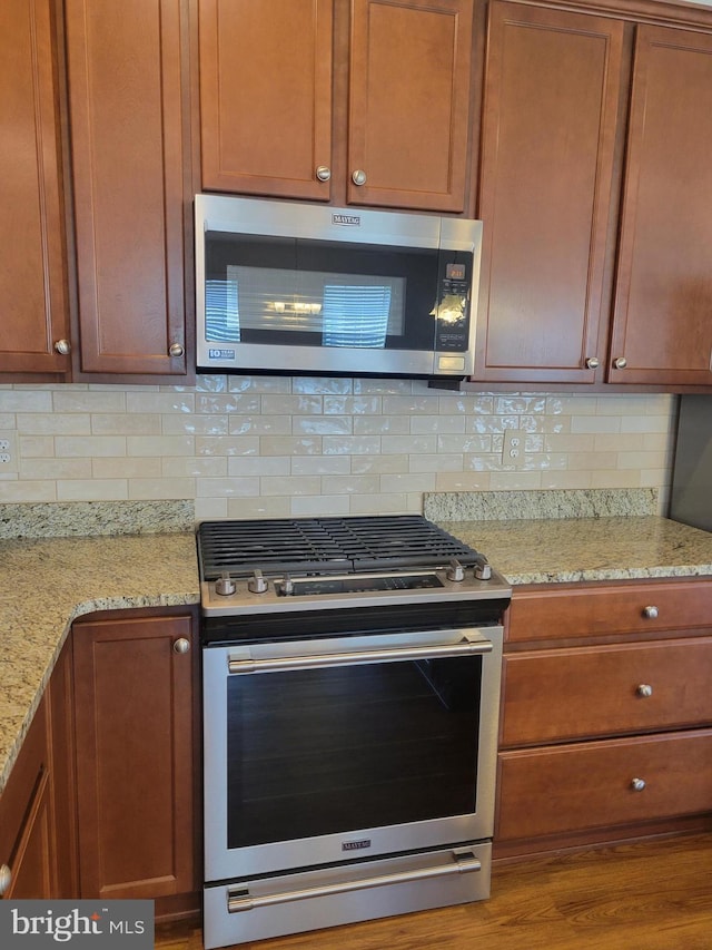 kitchen with stainless steel appliances, hardwood / wood-style flooring, backsplash, and light stone counters