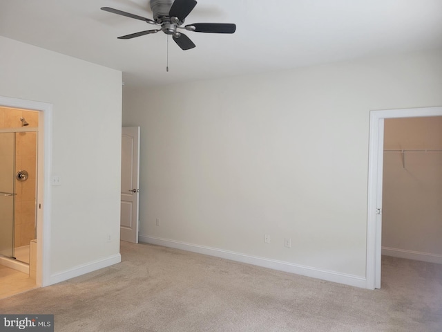 unfurnished bedroom featuring a walk in closet, connected bathroom, light carpet, and ceiling fan