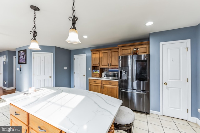 kitchen with appliances with stainless steel finishes, a breakfast bar area, light stone counters, hanging light fixtures, and light tile patterned floors