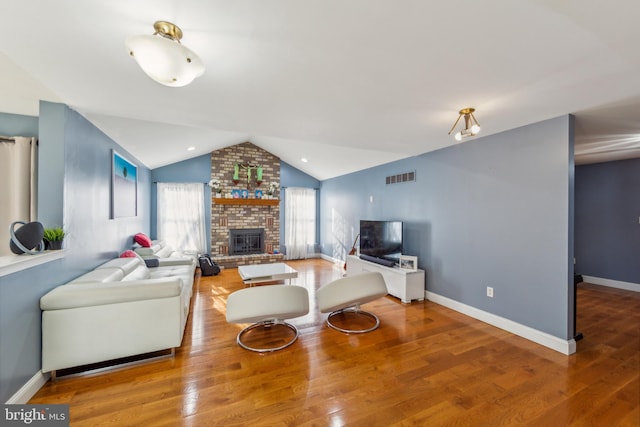 living room with brick wall, a brick fireplace, lofted ceiling, and hardwood / wood-style floors