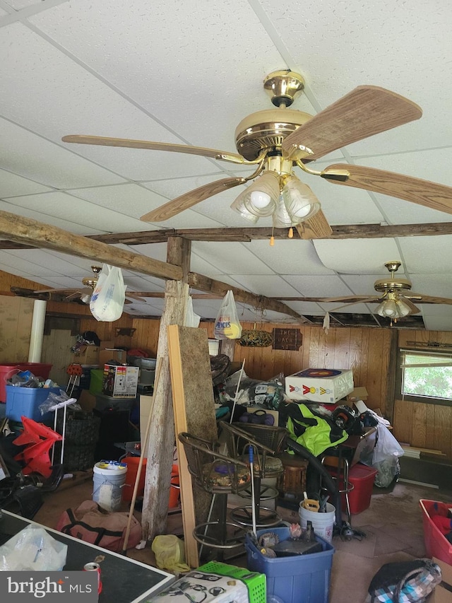 interior space with a paneled ceiling, wooden walls, and ceiling fan