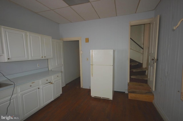 kitchen with dark hardwood / wood-style flooring, wooden walls, white cabinets, and white refrigerator