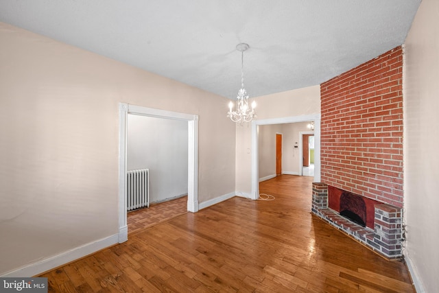 unfurnished dining area featuring a notable chandelier, a fireplace, hardwood / wood-style flooring, and radiator heating unit