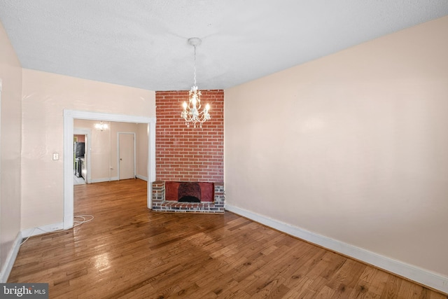 unfurnished living room featuring a brick fireplace, a chandelier, and hardwood / wood-style flooring