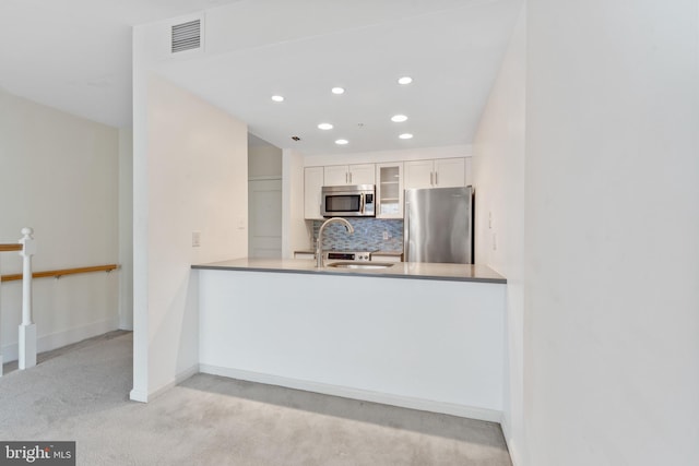 kitchen with backsplash, stainless steel appliances, light colored carpet, sink, and white cabinets