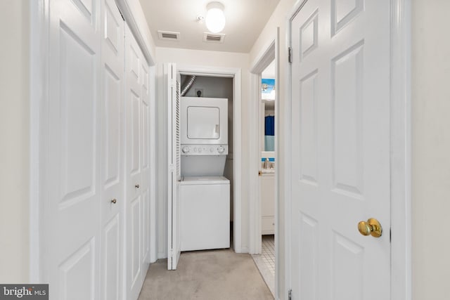 corridor with stacked washer / dryer and light carpet