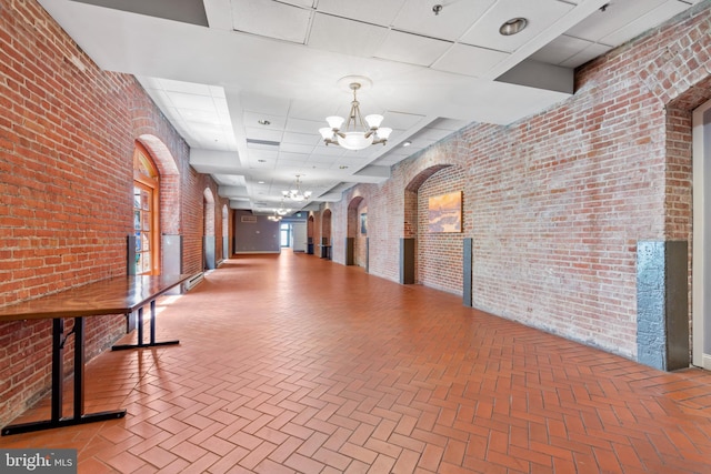 hall featuring a drop ceiling, a chandelier, and brick wall