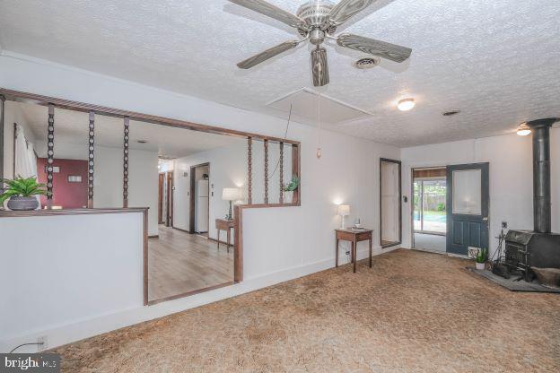 carpeted living room with ceiling fan, a textured ceiling, and a wood stove