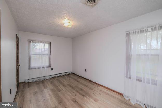 spare room with a textured ceiling, a baseboard heating unit, and light hardwood / wood-style flooring