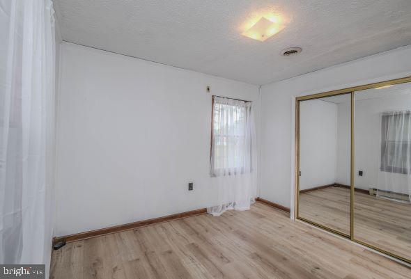 unfurnished bedroom featuring a textured ceiling, a closet, and light wood-type flooring