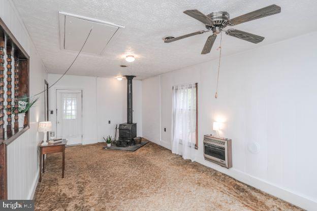 living room with carpet flooring, ceiling fan, a wood stove, heating unit, and a textured ceiling