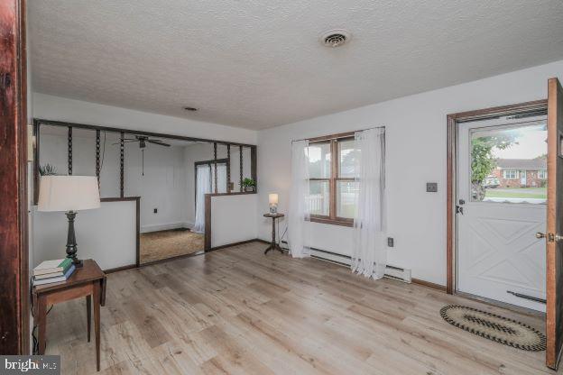 entryway featuring a baseboard heating unit, light wood-type flooring, and a textured ceiling