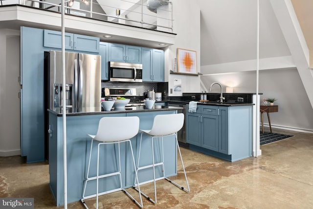 kitchen with appliances with stainless steel finishes, dark countertops, a high ceiling, and blue cabinetry