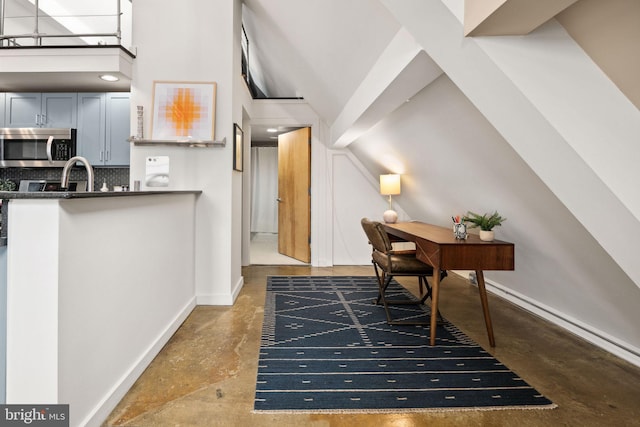 office space featuring concrete floors, a sink, a towering ceiling, and baseboards