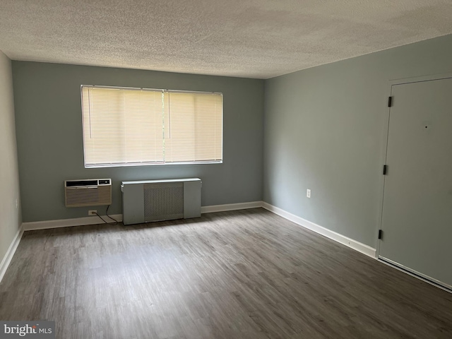 empty room featuring a wall mounted air conditioner, hardwood / wood-style flooring, a textured ceiling, and radiator