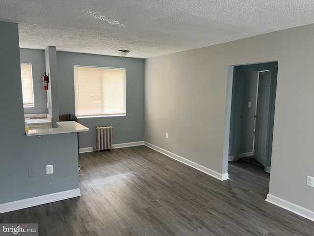 unfurnished living room with a textured ceiling, radiator heating unit, dark wood-type flooring, and plenty of natural light