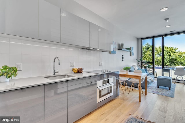 kitchen featuring a sink, gray cabinetry, expansive windows, and stainless steel oven