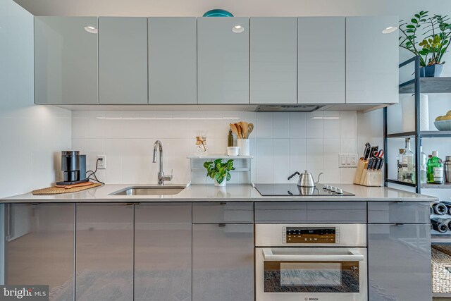 kitchen with gray cabinetry, oven, sink, decorative backsplash, and black electric cooktop