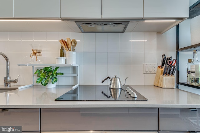 kitchen featuring white cabinets, light stone counters, sink, black electric stovetop, and tasteful backsplash