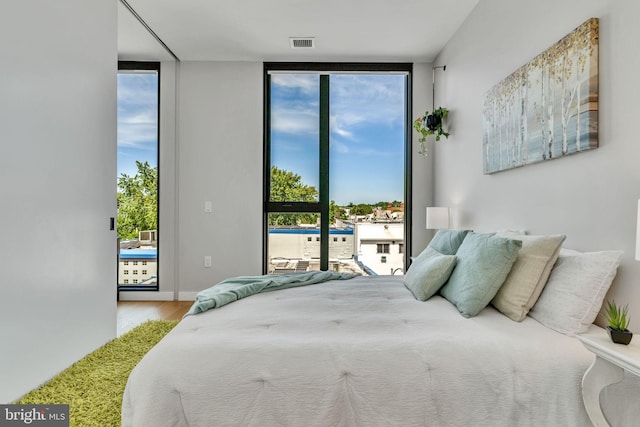 bedroom with a wall of windows, multiple windows, and light hardwood / wood-style flooring