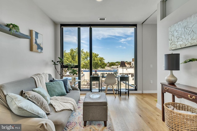 living room with a wall of windows, wood finished floors, visible vents, and baseboards