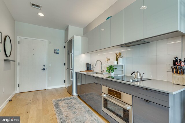 kitchen with stainless steel appliances, sink, decorative backsplash, and light hardwood / wood-style floors