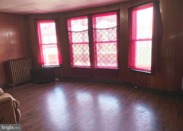 empty room with hardwood / wood-style flooring, a drop ceiling, wood walls, and radiator heating unit