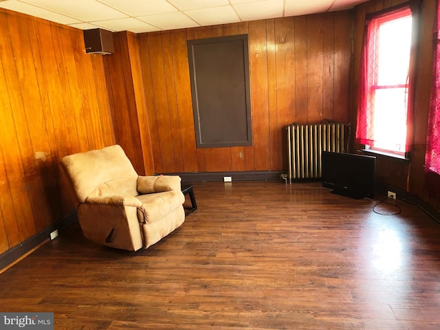 sitting room with a paneled ceiling, wood walls, radiator heating unit, and dark wood-type flooring