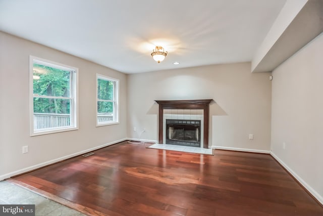 unfurnished living room featuring wood-type flooring and a tiled fireplace