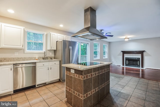 kitchen featuring white cabinets, island exhaust hood, stainless steel appliances, sink, and a tile fireplace