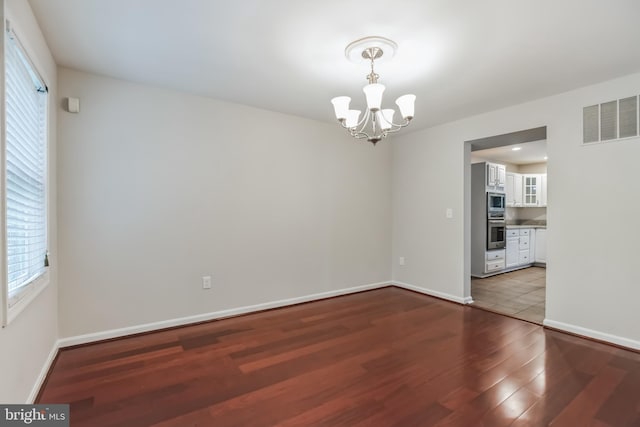 unfurnished room with wood-type flooring, a wealth of natural light, and a chandelier