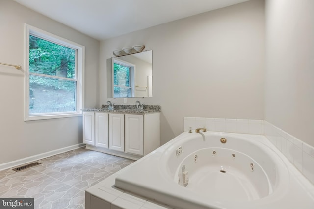 bathroom featuring a wealth of natural light, tiled tub, and vanity