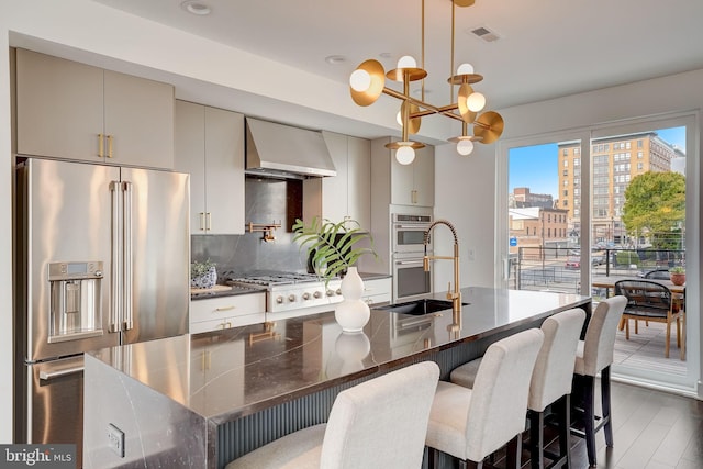 kitchen featuring a center island with sink, sink, wall chimney exhaust hood, appliances with stainless steel finishes, and tasteful backsplash