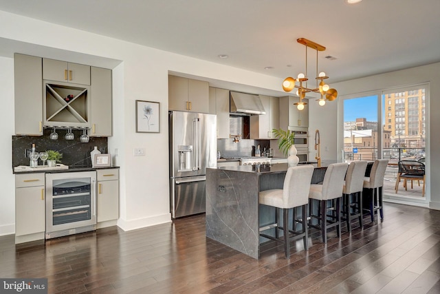 kitchen with appliances with stainless steel finishes, backsplash, beverage cooler, wall chimney range hood, and pendant lighting