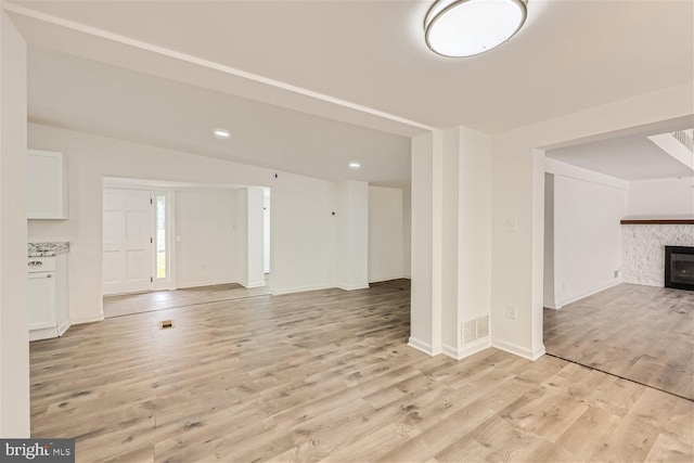 unfurnished living room with a stone fireplace and light wood-type flooring