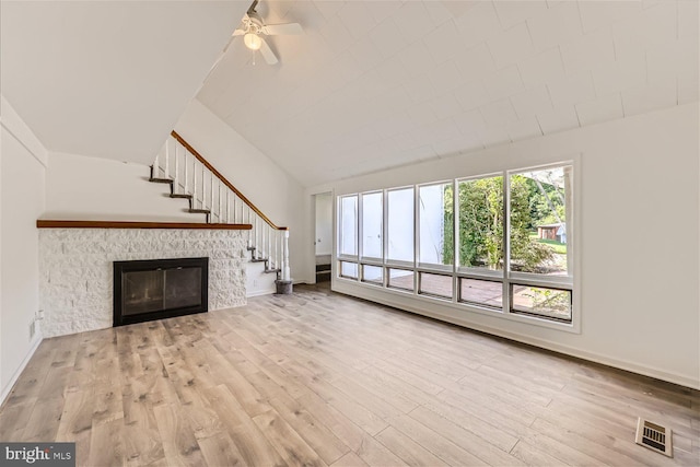 unfurnished living room with ceiling fan, a stone fireplace, and light wood-type flooring