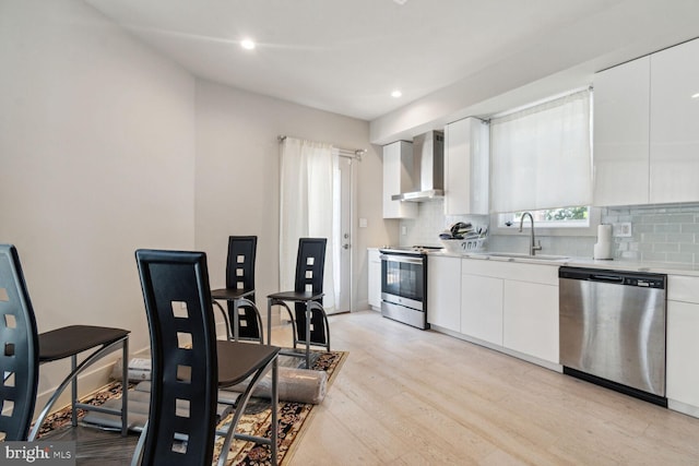 kitchen with decorative backsplash, sink, appliances with stainless steel finishes, white cabinets, and wall chimney exhaust hood