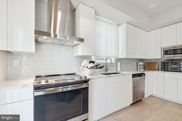 kitchen with white cabinetry, wall chimney range hood, stainless steel appliances, light hardwood / wood-style floors, and sink