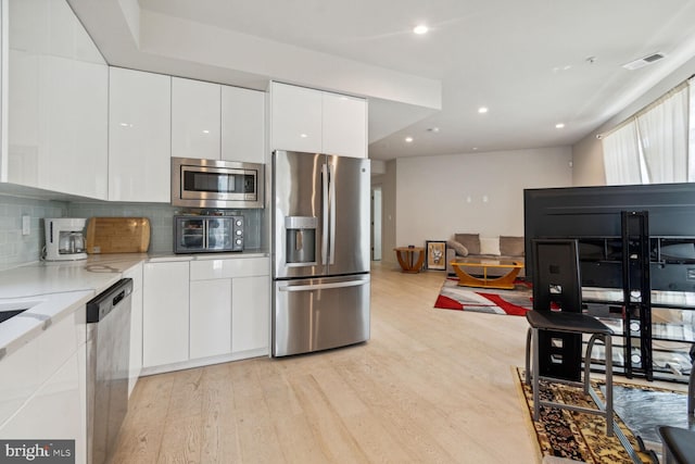 kitchen featuring light hardwood / wood-style floors, white cabinets, backsplash, and appliances with stainless steel finishes