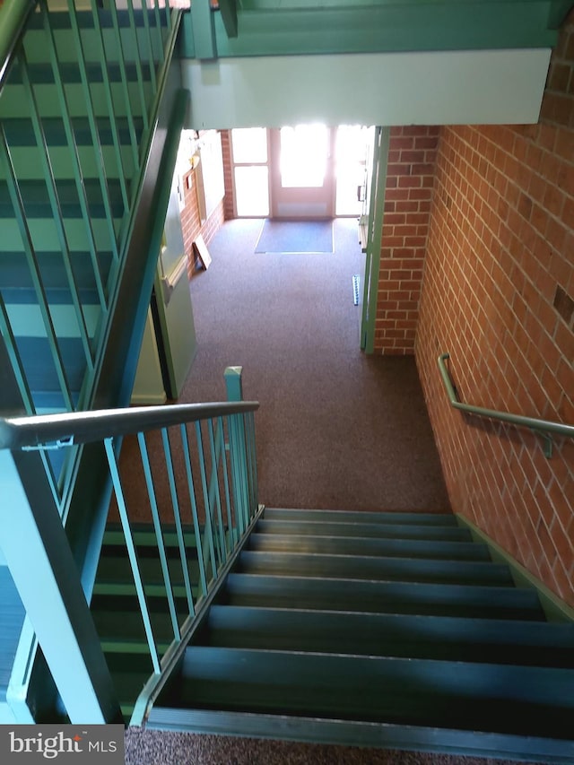 stairway featuring carpet floors and brick wall