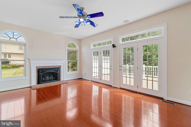 unfurnished living room featuring french doors, ceiling fan, a brick fireplace, and light wood-type flooring