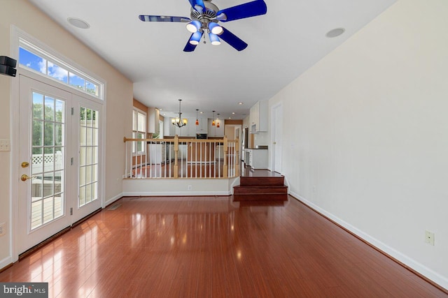 unfurnished living room with ceiling fan with notable chandelier and hardwood / wood-style floors