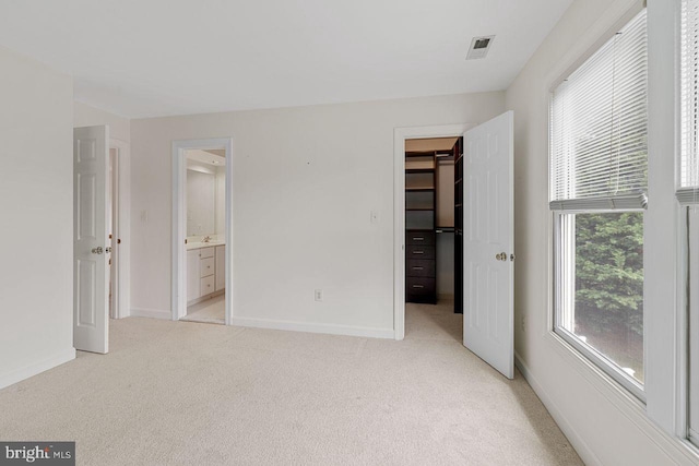 unfurnished bedroom featuring a closet, a walk in closet, light colored carpet, and ensuite bath