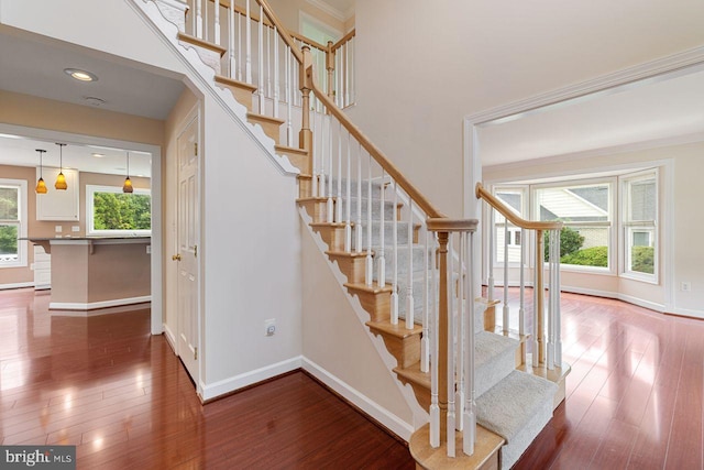 staircase with crown molding, wood-type flooring, and a chandelier