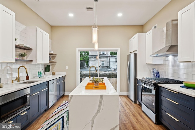 kitchen with appliances with stainless steel finishes, white cabinetry, hanging light fixtures, and wall chimney exhaust hood